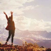mujer feliz levantando las manos en la montaña