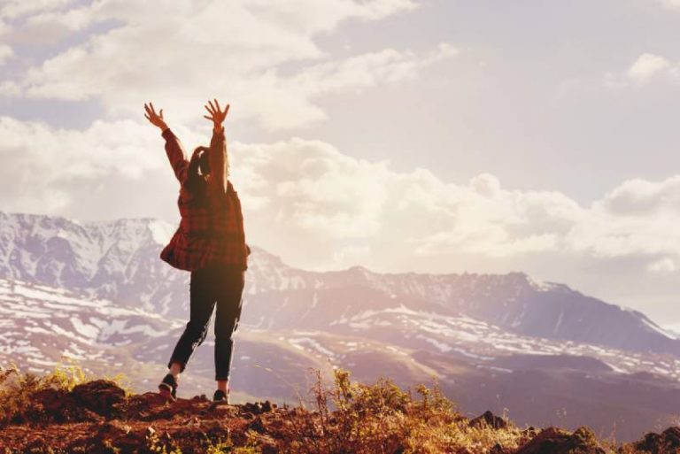 happy woman raising hands up on mountain