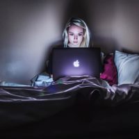 woman sitting on bed while using laptop