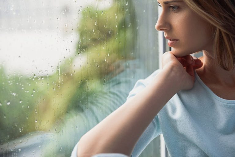 sad woman looking through the rainy window