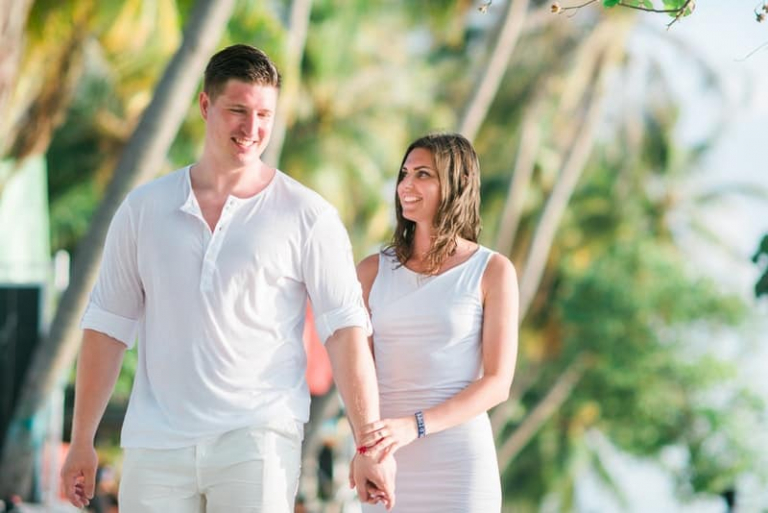 man and woman wearing white walking along the tropical beach