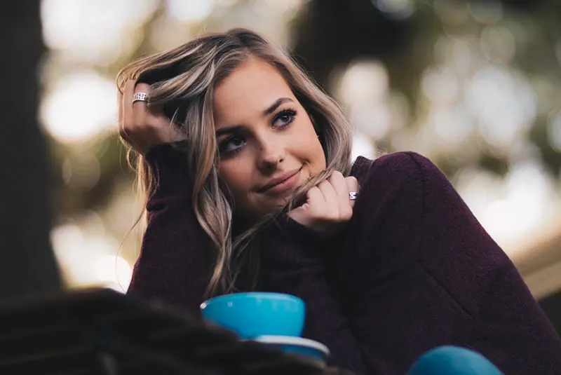 Smiling woman clasps hair and chin while thinking