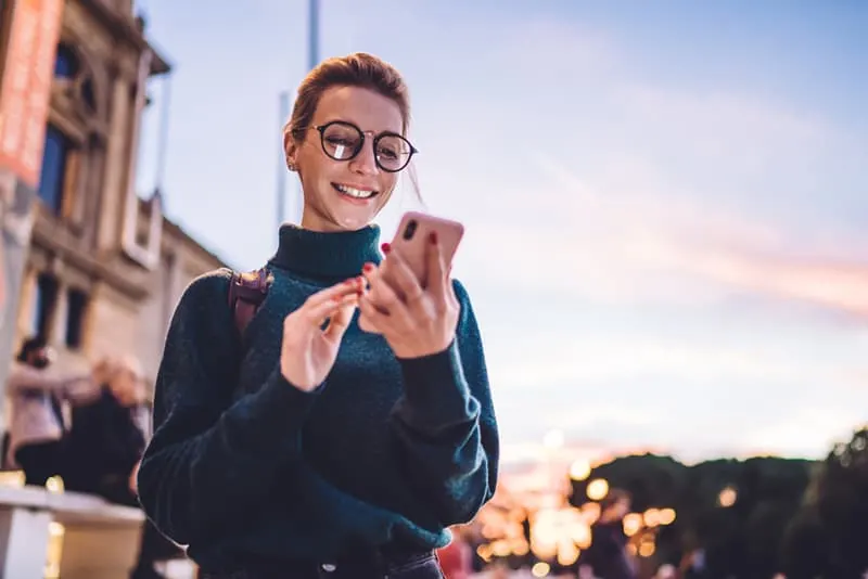 Woman in turtleneck and wearing glasses smiling at her phone