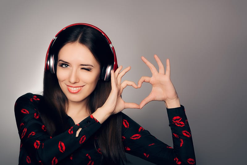 Winking woman with headphones on and making heart sign with hands
