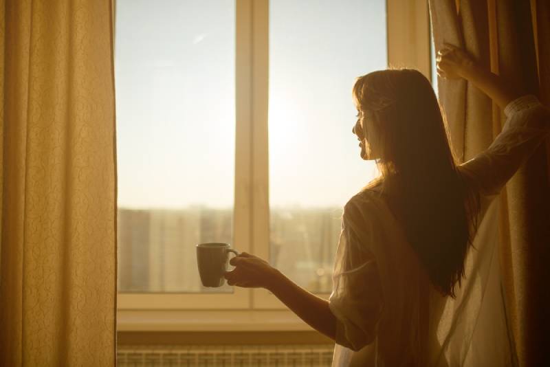 Woman holds a cup of hot tea and looks at the sunrise