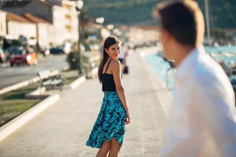 woman in blue dress looks back at man