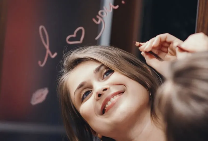 Woman smiling with I Love You written above reflection in mirror 