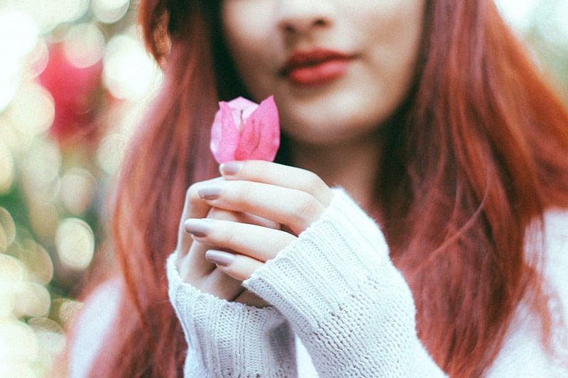 Donna con giacca bianca in cashmere che tiene in mano un bocciolo di fiore rosa