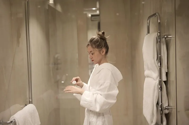 Woman inside bathroom wearing bathrobe and putting on Lotion on hands