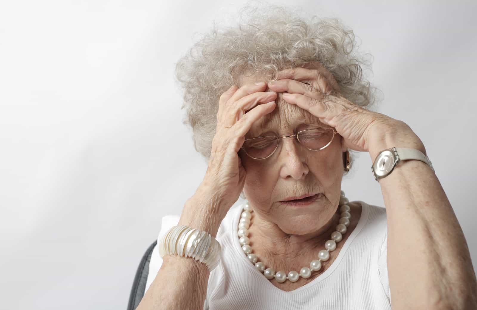 woman with headache holding her head wearing white top