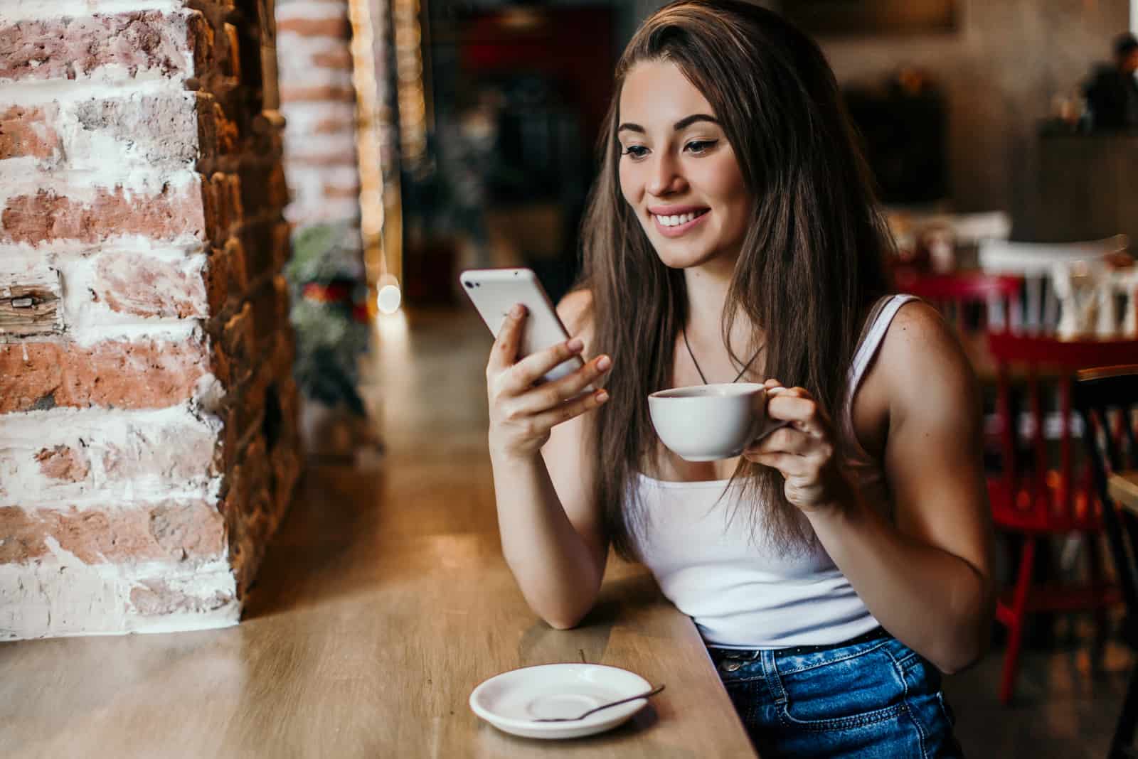 a beautiful young woman with long brown hair drinks coffee and keys on the phone