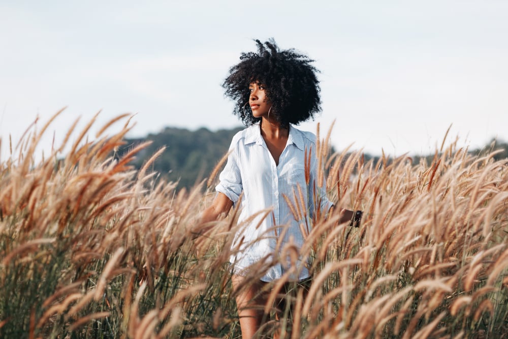 uma mulher negra com uma camisa branca caminha por um campo de trigo