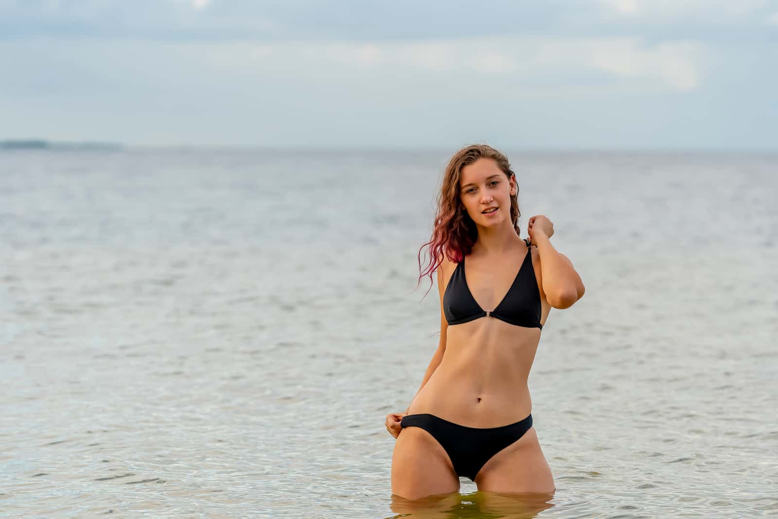 una donna dai capelli castani seduta nell'acqua in bikini