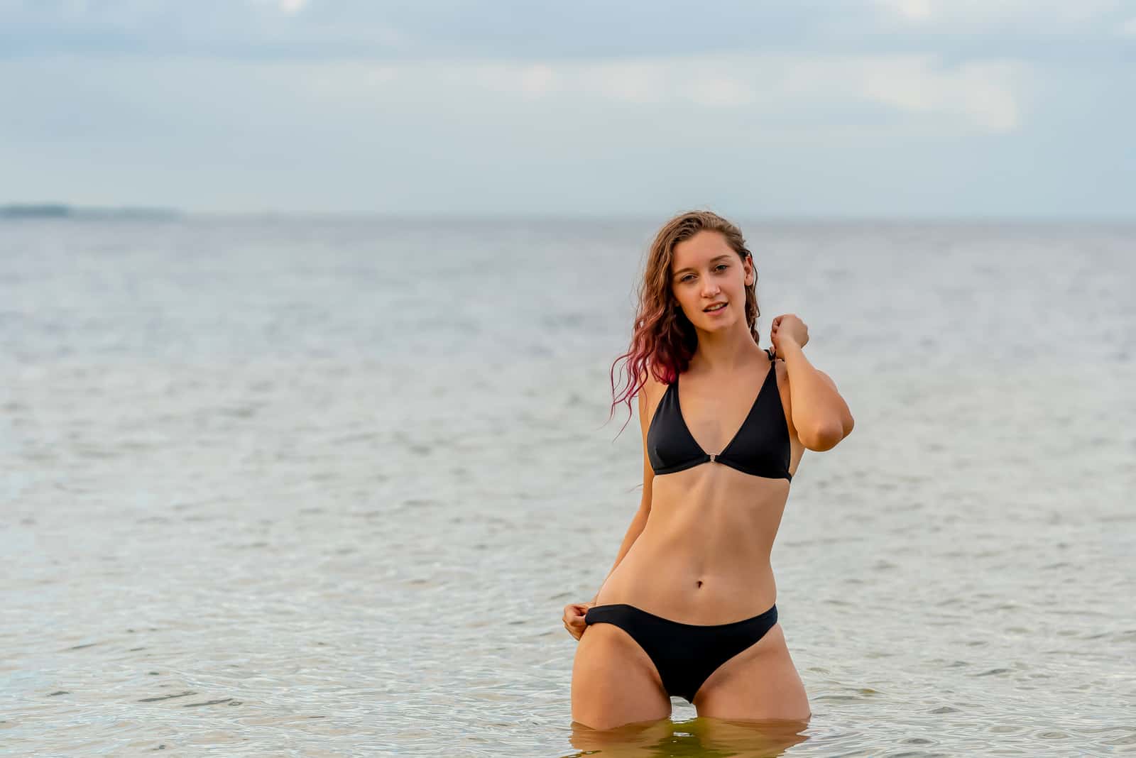 a brown-haired woman sitting in the water in a bikini