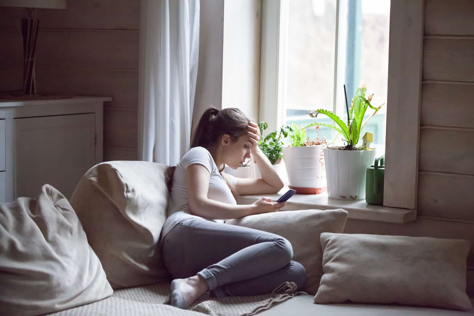 a disappointed woman sits on the couch and holds the phone in her hand