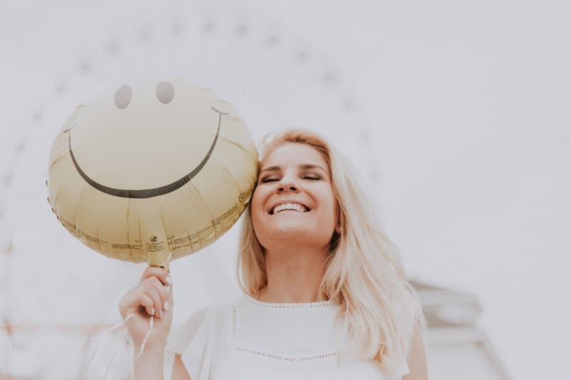 a happy woman in white top holding a smiley balloon