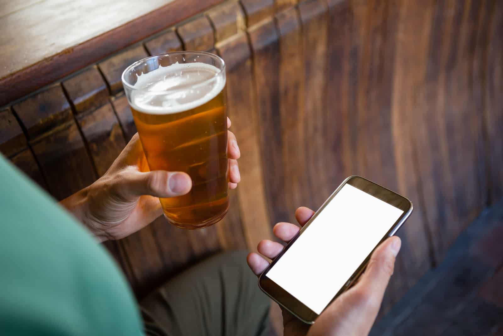 a man drinks a beer and holds a phone in his hand