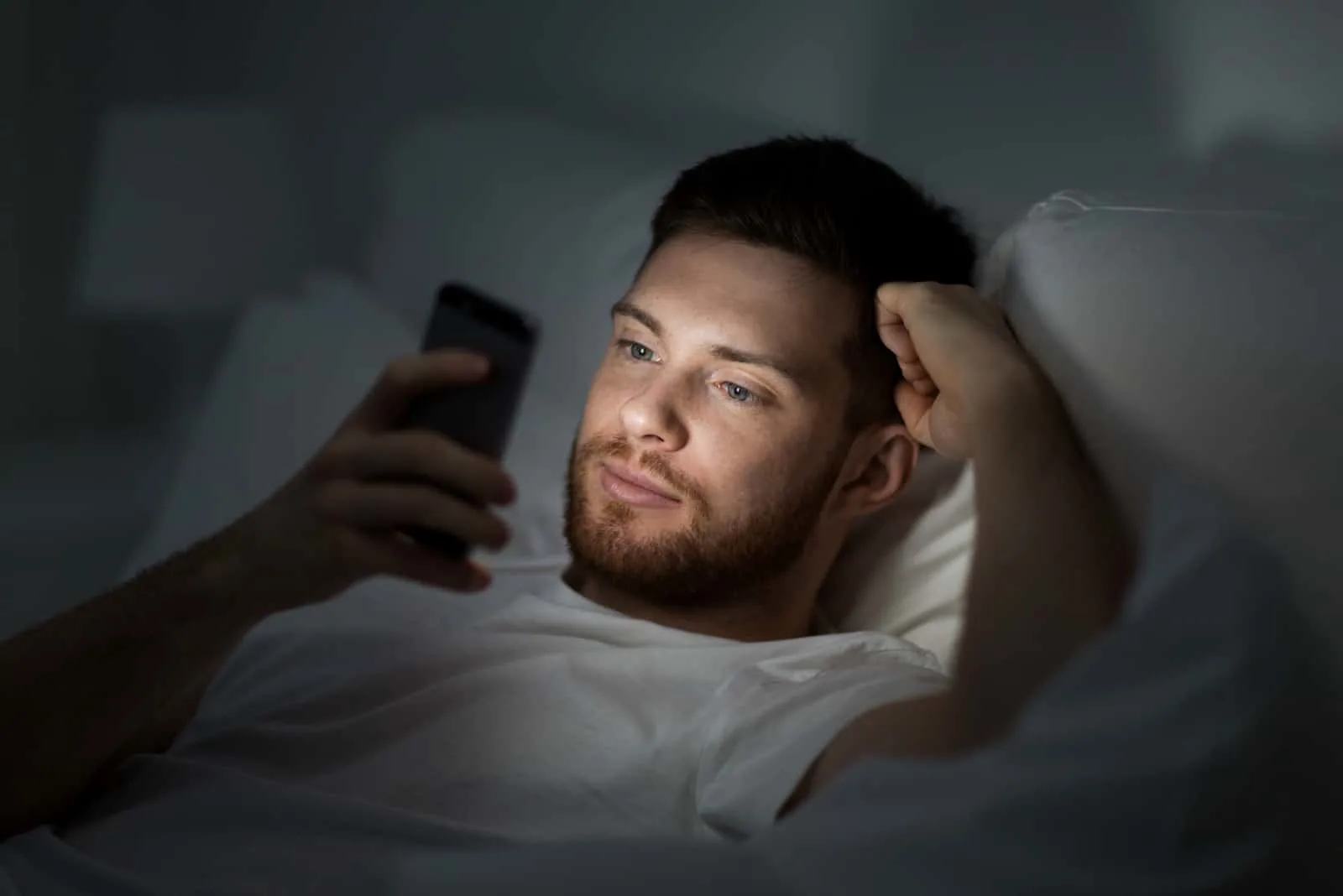 a man lies in bed and keys on the phone