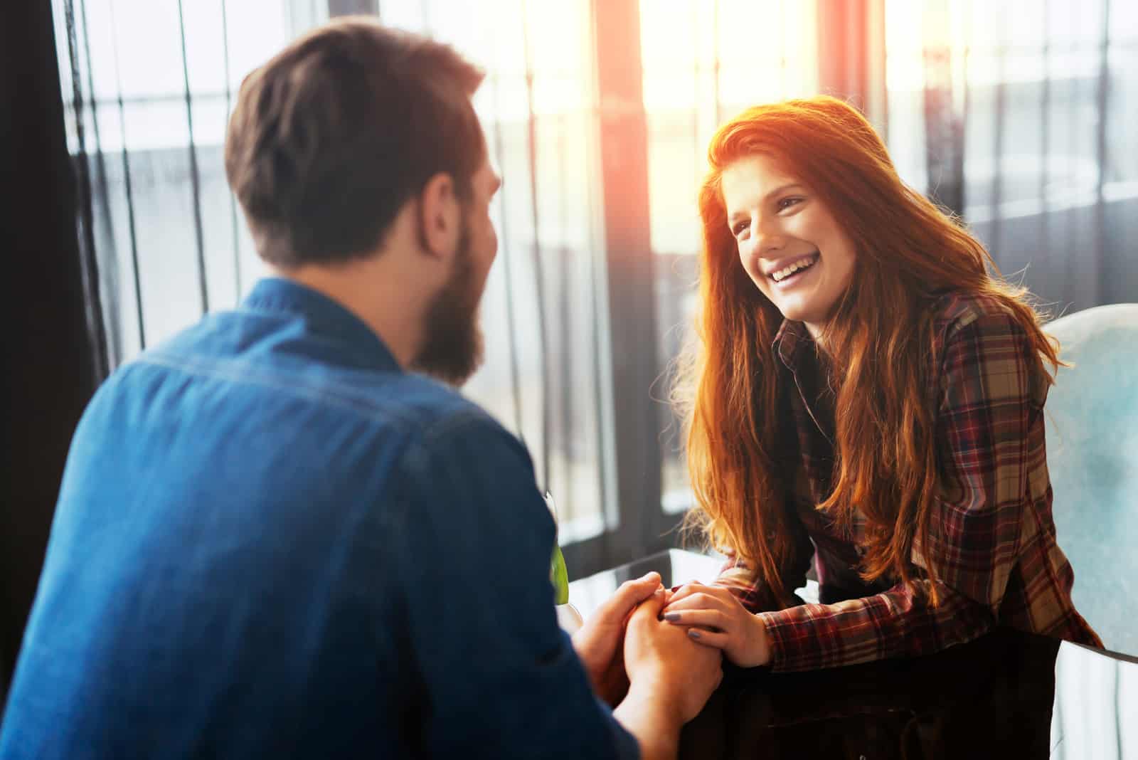 una pareja sonriente sentada a la mesa riendo y cogida de la mano