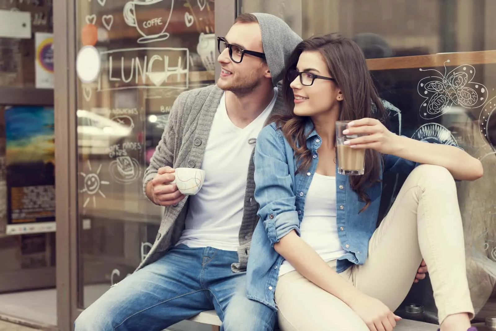 a smiling couple sitting drinking coffee and looking away
