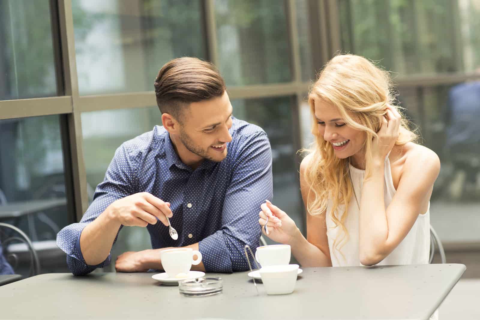 um casal sorridente sentado ao ar livre a beber café e a rir