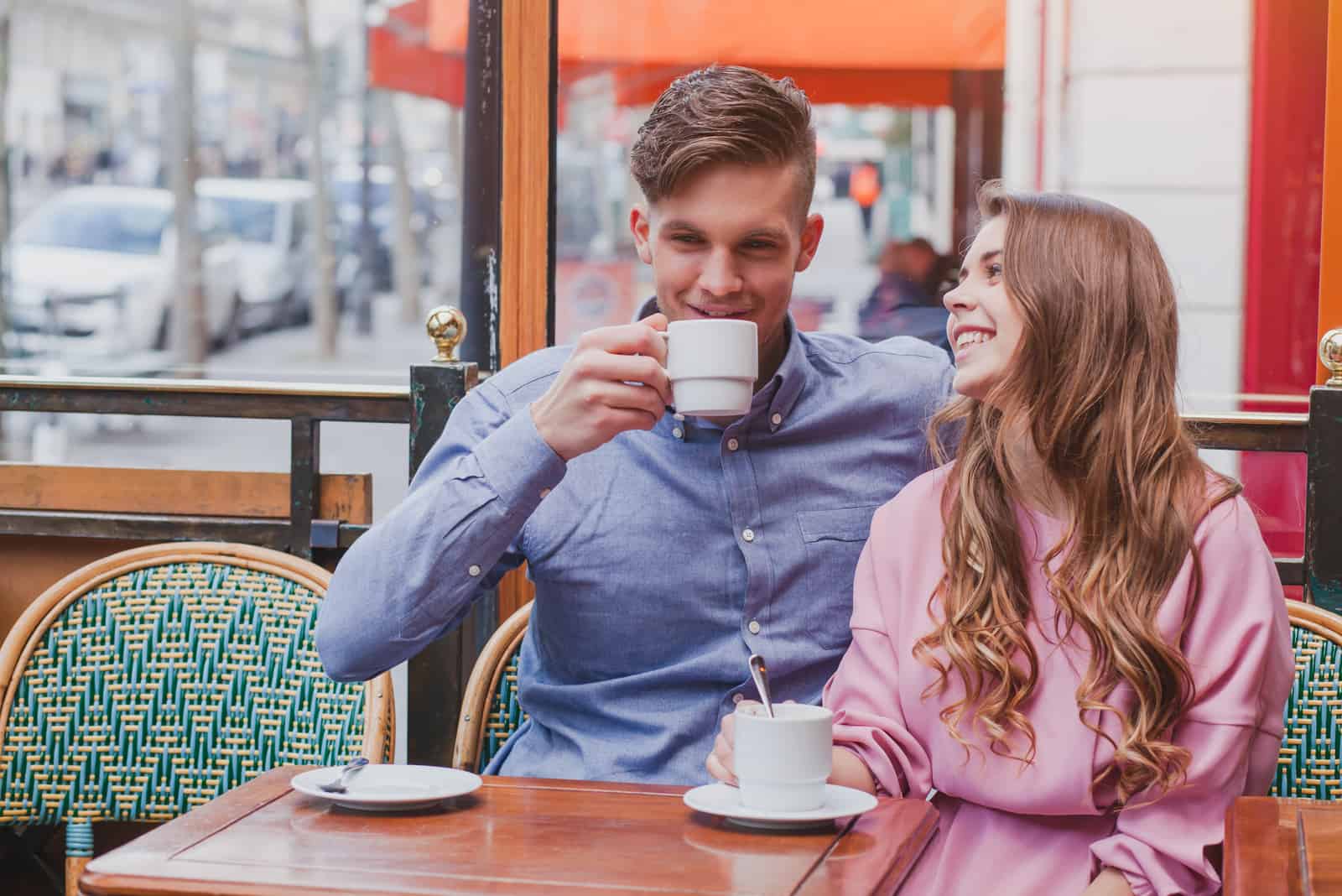 a smiling man and woman sitting drinking coffee outdoors