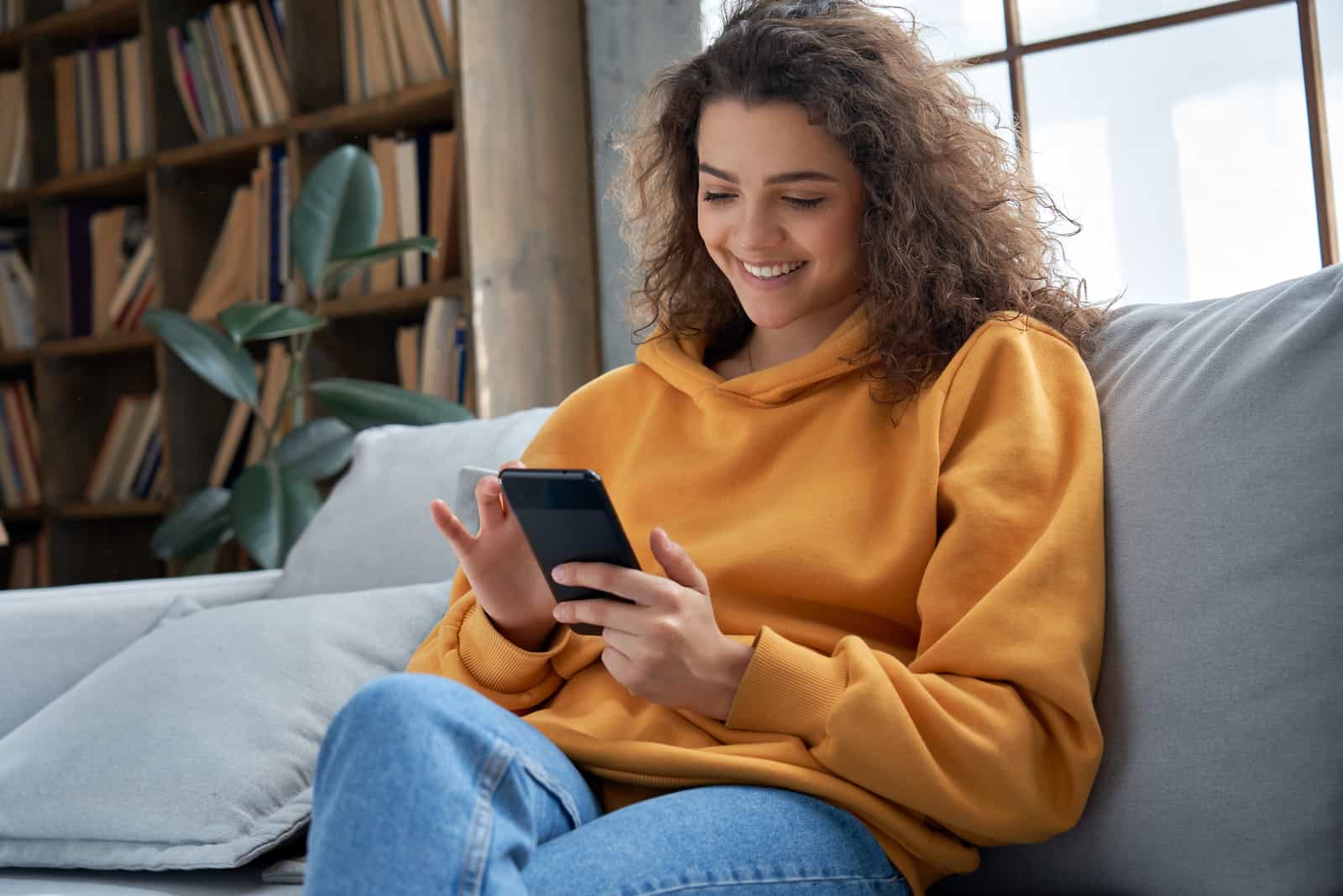 a smiling woman sits on the couch and keys on the phone