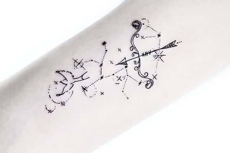 uma tatuagem única de um pequeno arco e de um pássaro rodeado de estrelas