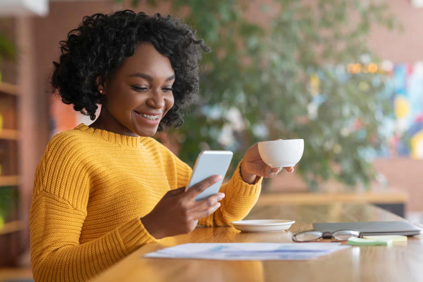 a woman with frizzy hair sitting drinking coffee and pressing a phone