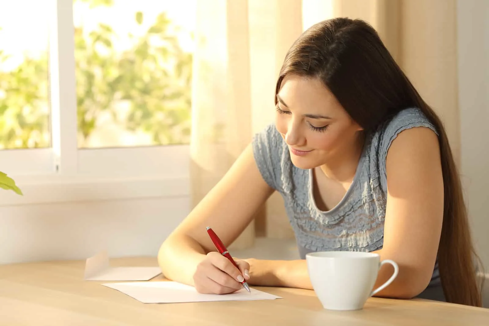 a woman with long brown hair sits writing a letter