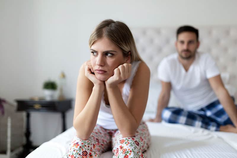 angry woman sitting on the bed distanced from man