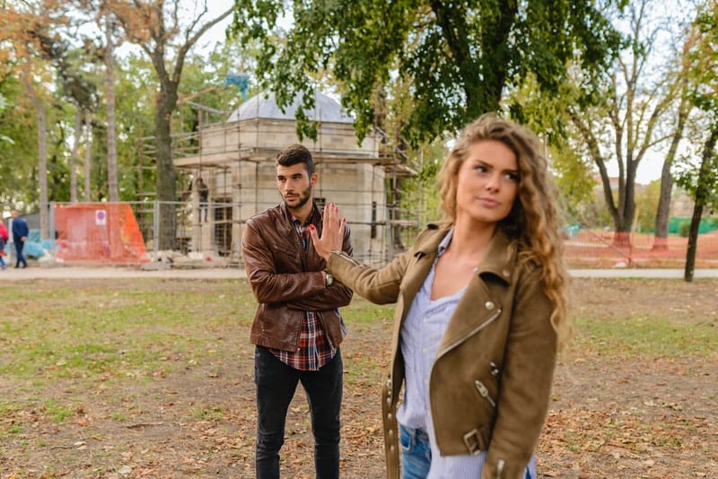 arguing man and woman wearing jackets standing in the park