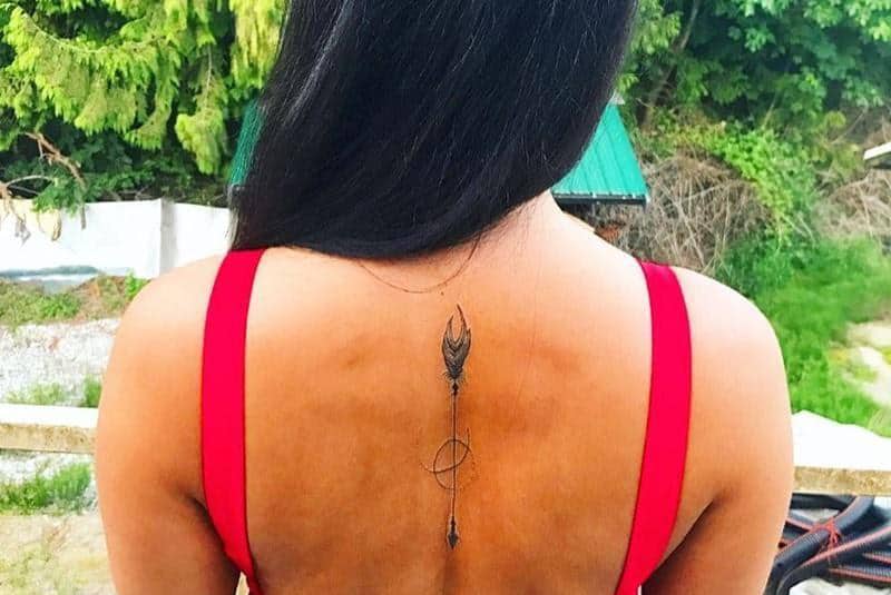 tatuagem de uma seta com o símbolo de um planeta nas costas de uma mulher