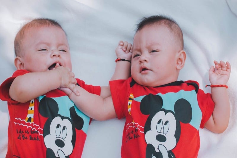 two babies with red mickey mouse shirts laying on bed
