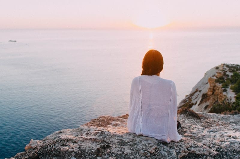 vista posteriore di una donna seduta su uno scoglio che guarda il mare