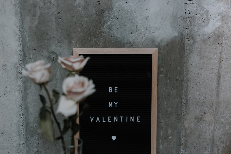 messaggio "be my valentine" su lavagna nera con rose a fianco