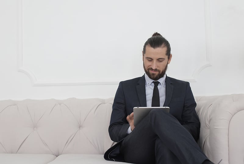 beard man in black suit sitting on white couch