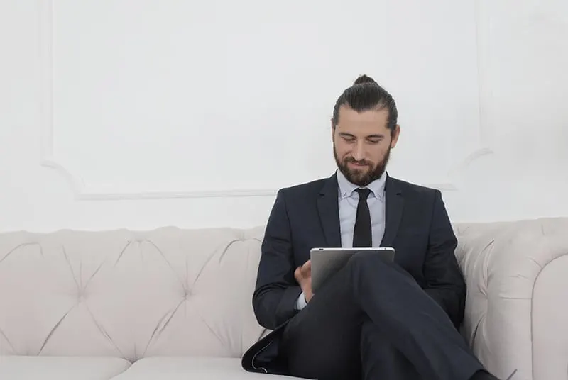 beard man in black suit sitting on white couch