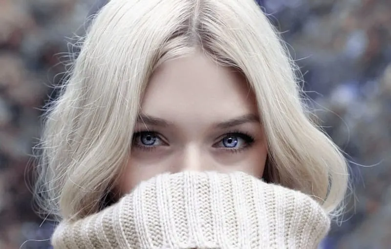 beautiful blond woman covering her mouth with her sweater in focus photography
