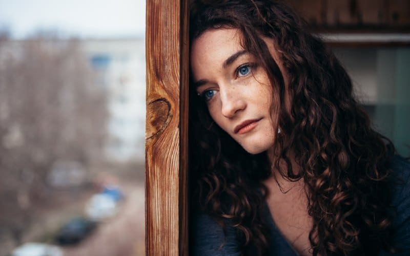 hermosa chica triste y solitaria sentada cerca de la ventana durante el día