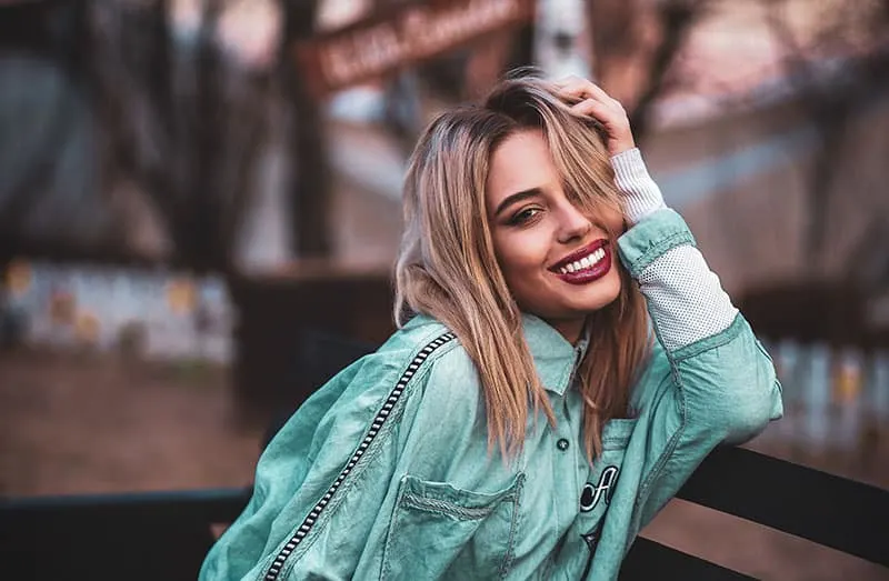 beautiful smiling woman leaning on bench wearing denim jacket