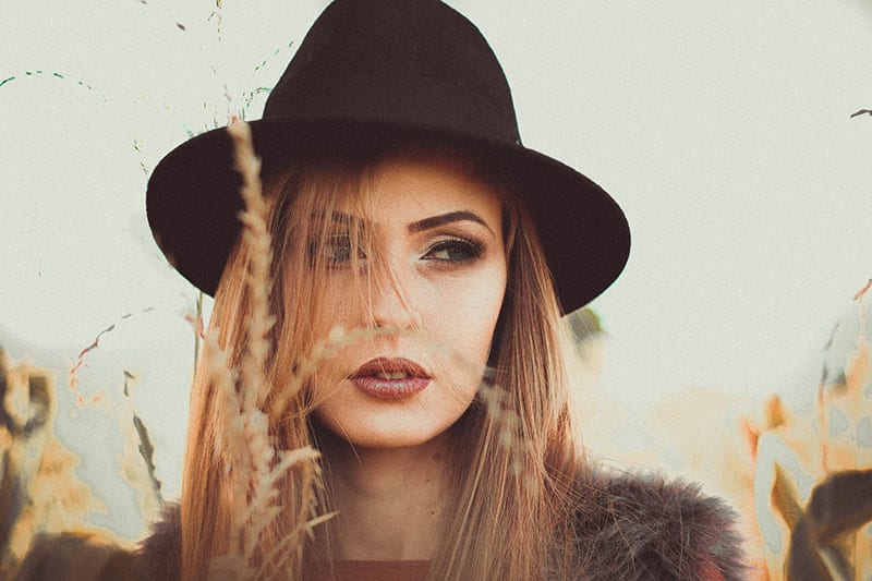 beautiful woman with hat with tall grass in front of her