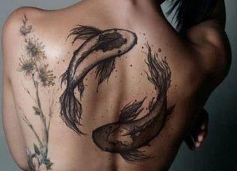 bold black pisces tattoo on woman`s back