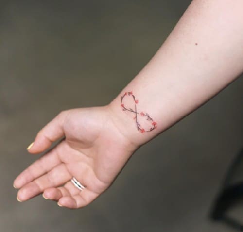 Tatuaggio botanico minimale con dettagli rossi sul polso
