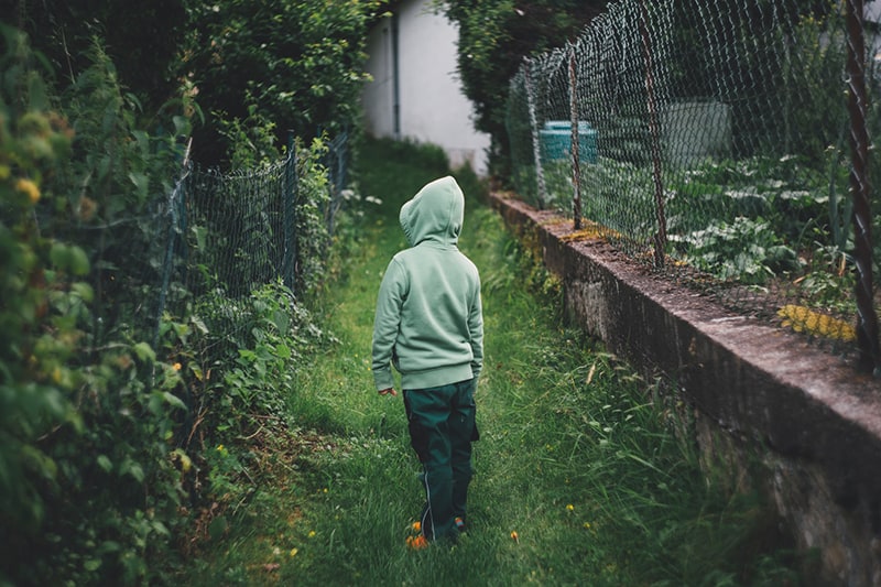 boy standing on grass and facing fence