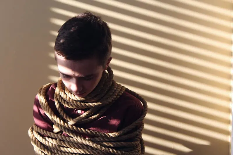boy tied with a rope with shadows of the blinds from a window