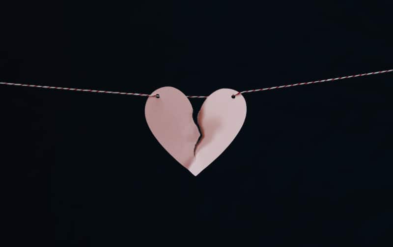 Broken pink heart hanging on red and white wire on a black background