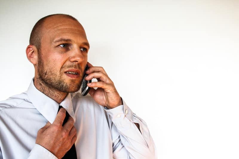 hombre de negocios llamando por teléfono con una mano en la corbata