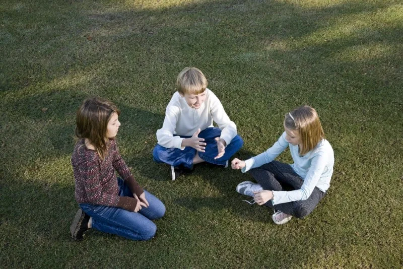 three kids sitting on grass and talking
