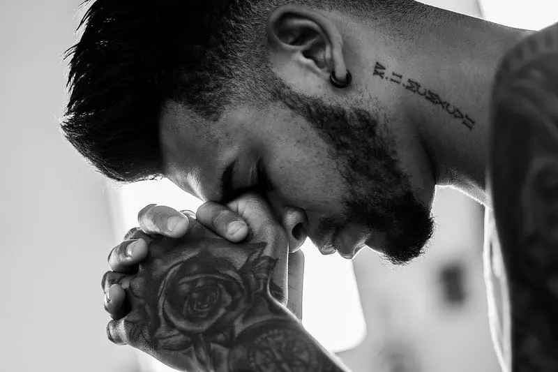 close up photo of tattooed man praying in grayscale